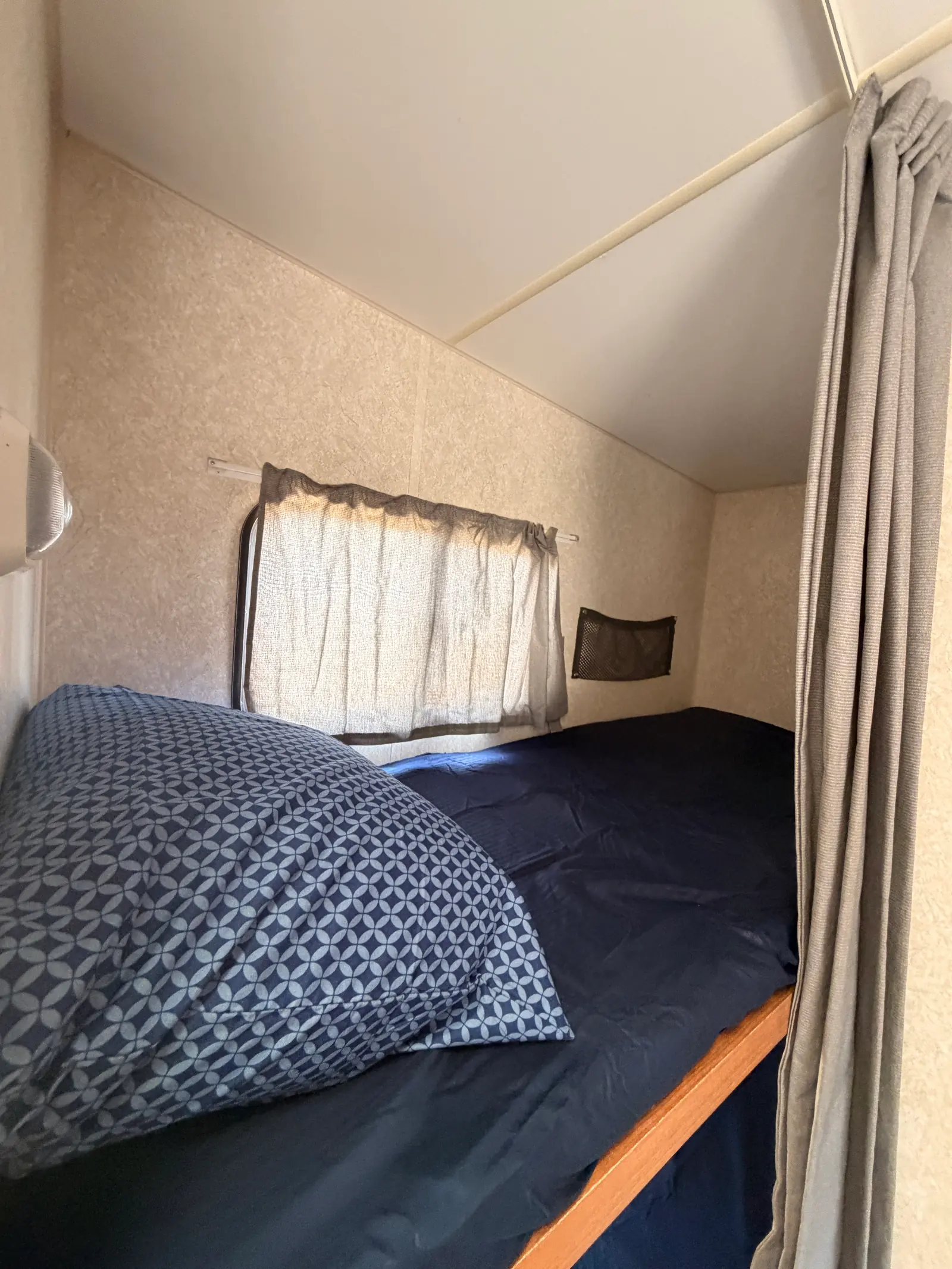Lower bunk made up with a navy comforter and pillow beside its own window