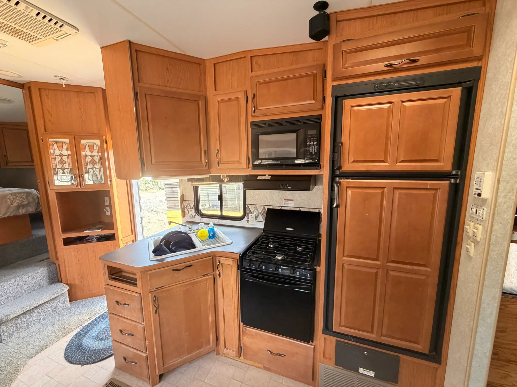 Full RV kitchen with a double-door refrigerator, three-burner gas range, oven, microwave and sink
